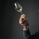 Enólogo examina cuidadosamente uma taça de vinho branco em ambiente de degustação.