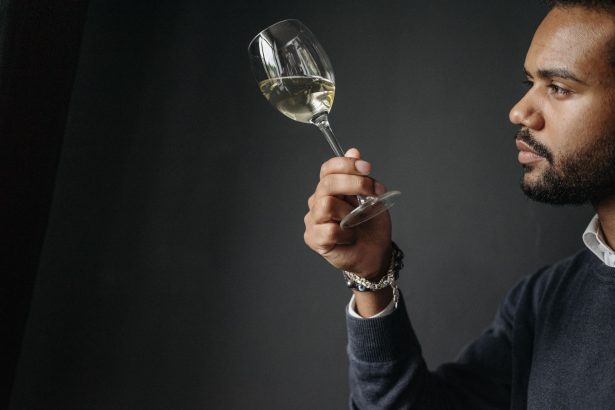 Enólogo examina cuidadosamente uma taça de vinho branco em ambiente de degustação.