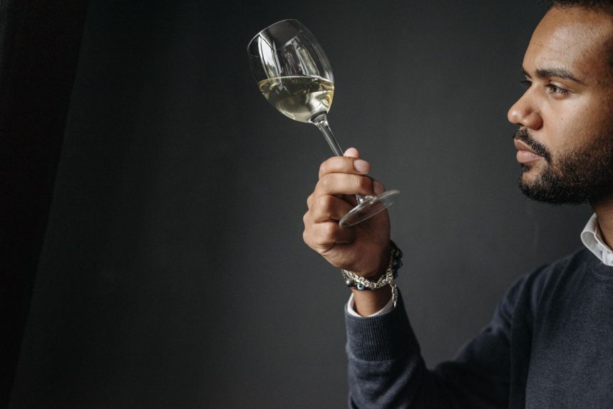 Enólogo examina cuidadosamente uma taça de vinho branco em ambiente de degustação.