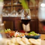 Taça de vinho tinto entre pratos variados sobre uma mesa de restaurante.