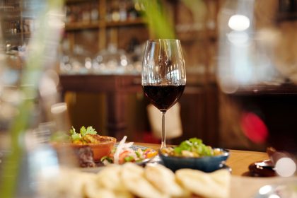 Taça de vinho tinto entre pratos variados sobre uma mesa de restaurante.